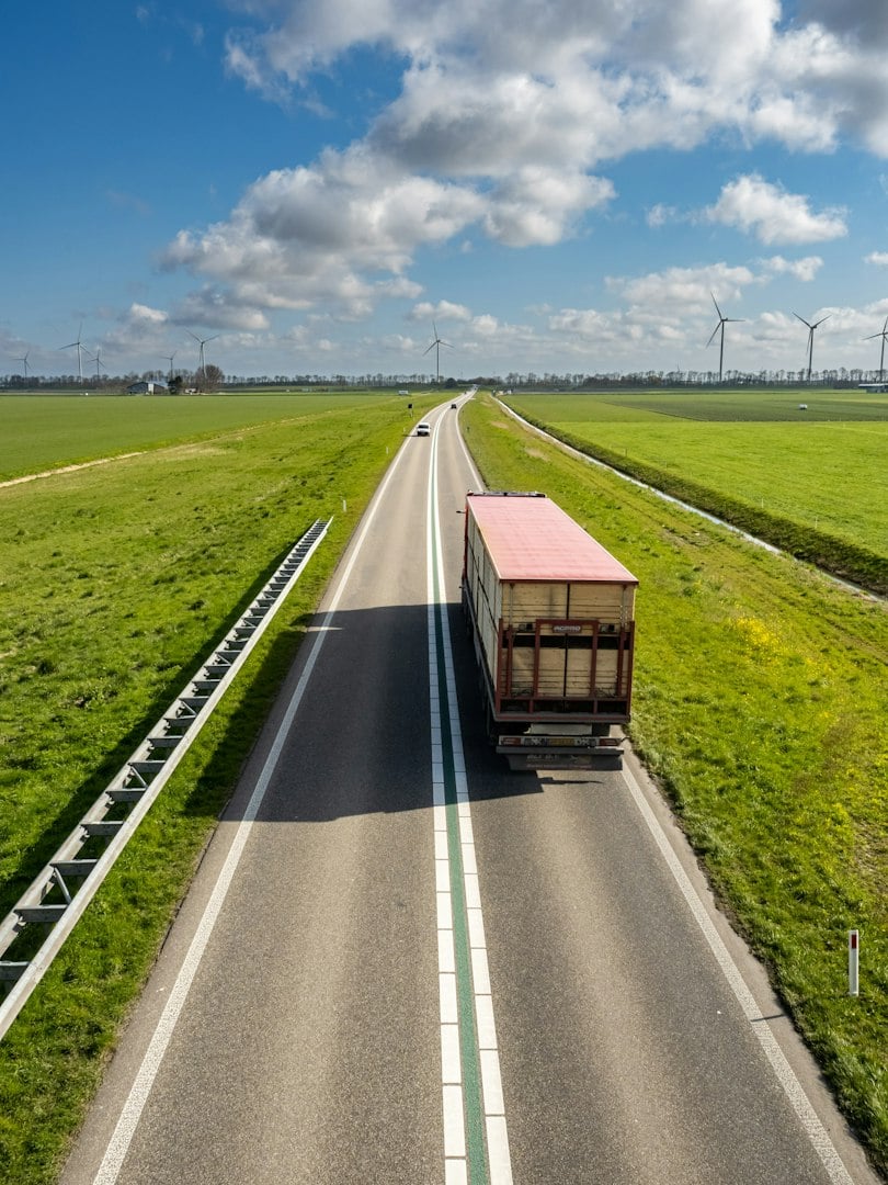Freight truck hauls shipping container. Freight transport crosses highway bridge. Container freight moves through route. Commercial freight supports supply chain